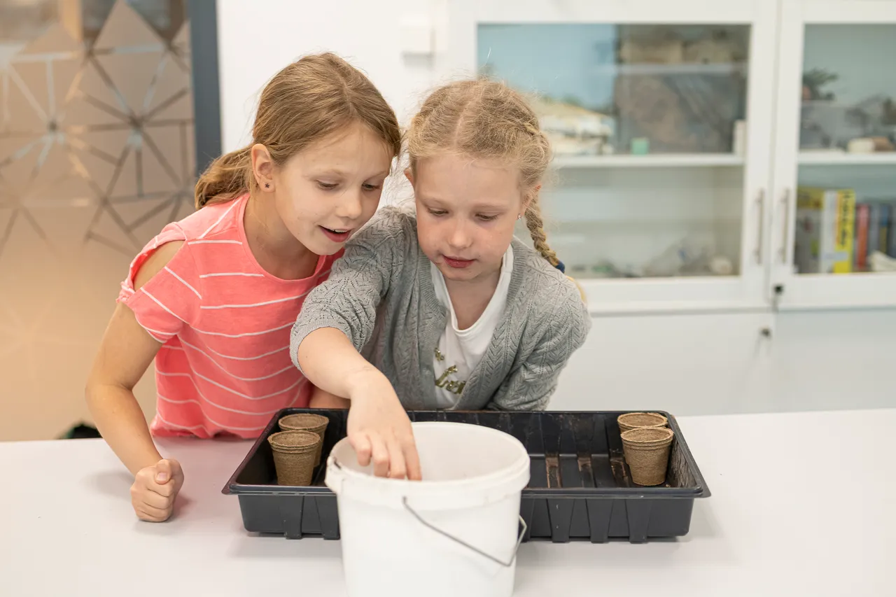Two girls planting vegetables in classroom