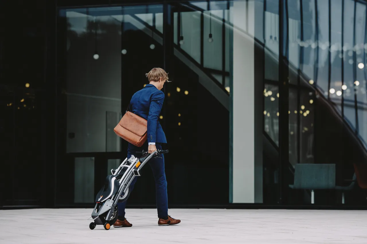 Man walking with a foldable elecric bike in front of office