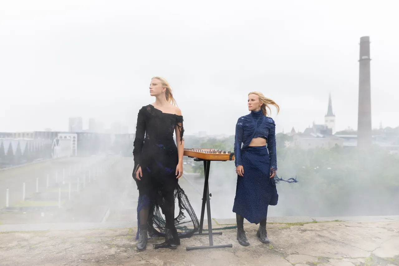 Two women from Duo Ruut, Katariina Kivi and Ann-Lisett Rebane, playing kannel outdoors in a misty urban setting.