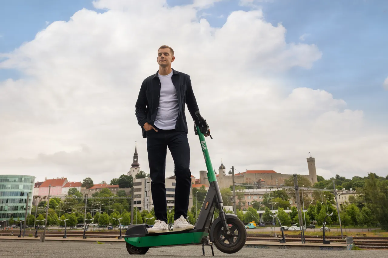 Markus Villig sitting with a Bolt e-scooter in front of Tallinn cityscape.