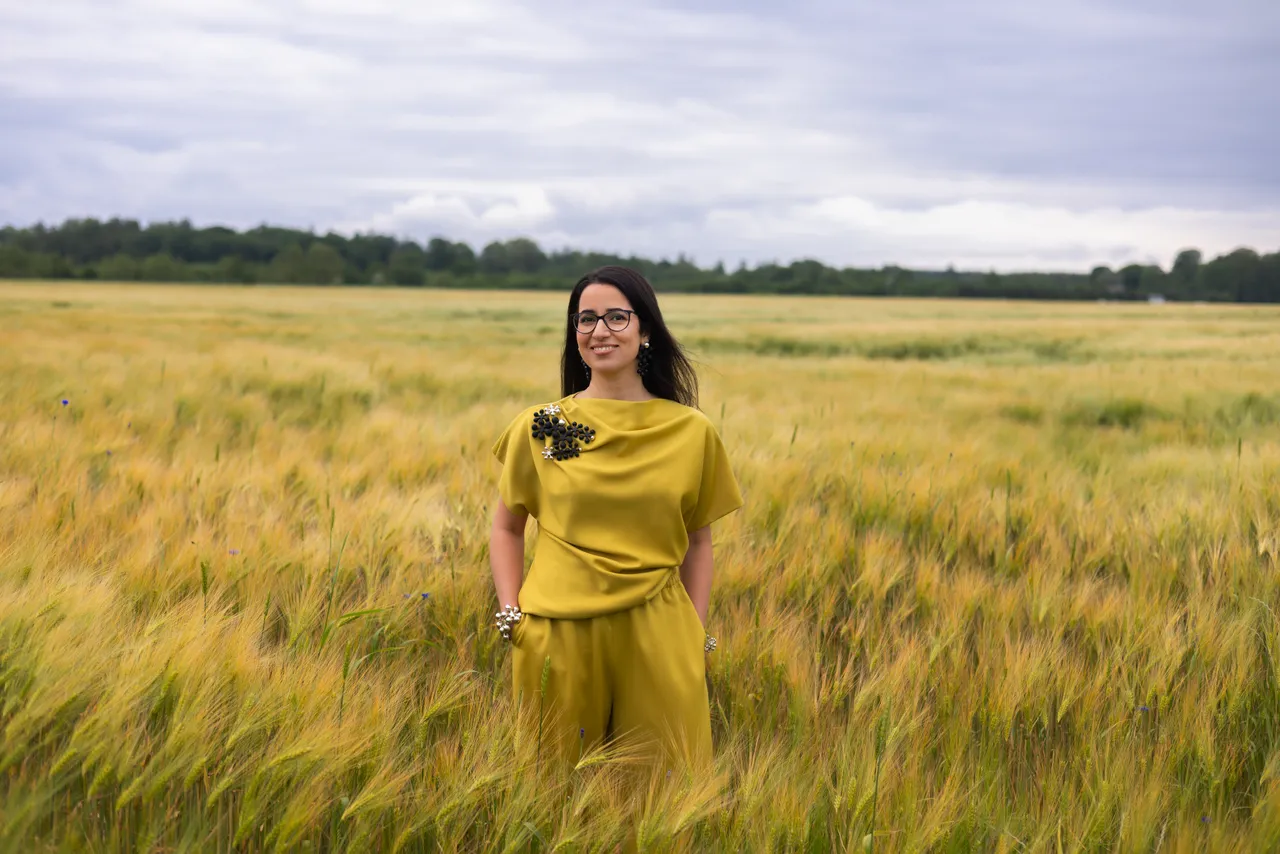 Lili Milani standing in a summer grain field wearing a yellow outfit