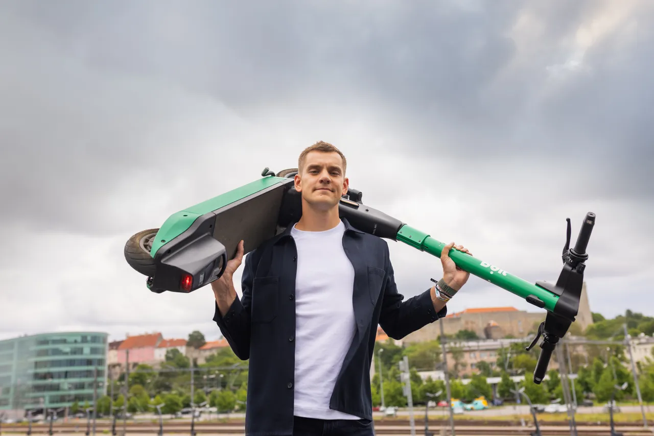 Markus Villig sitting with a Bolt e-scooter in front of Tallinn cityscape.