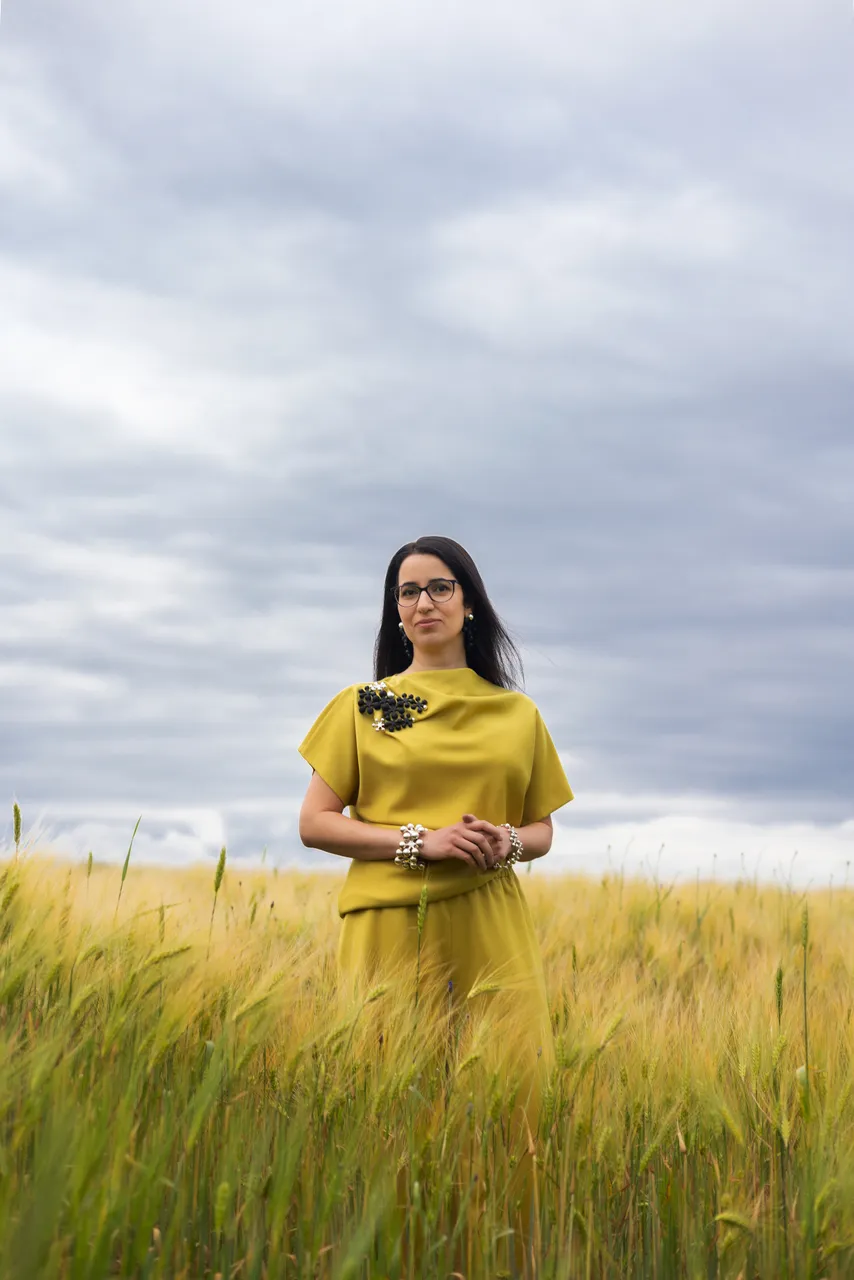 Lili Milani standing in a summer grain field wearing a yellow outfit