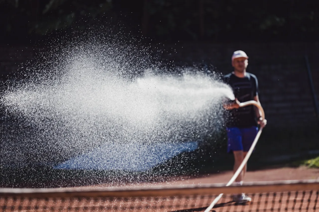Man watering tennis court