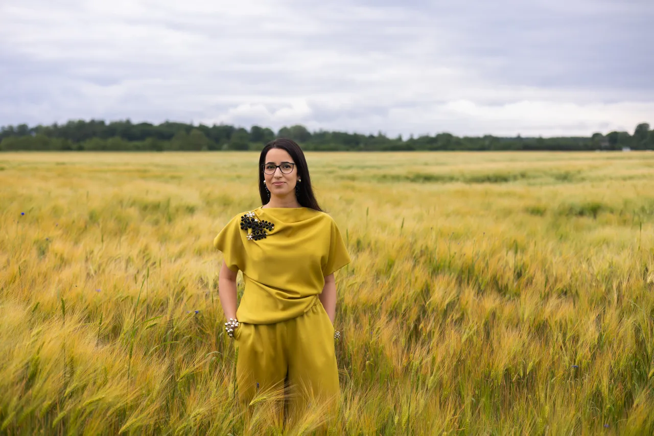 Lili Milani standing in a summer grain field wearing a yellow outfit