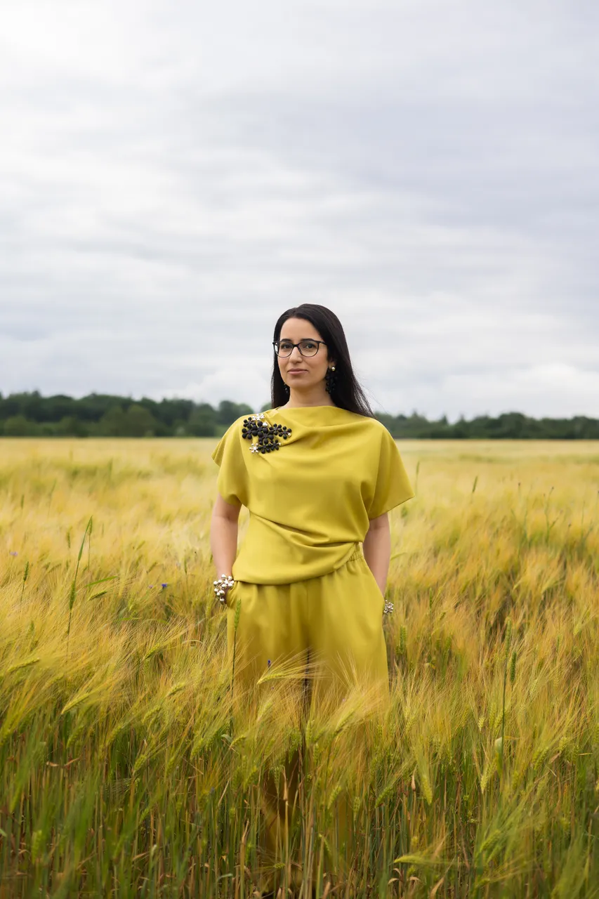 Lili Milani standing in a summer grain field wearing a yellow outfit