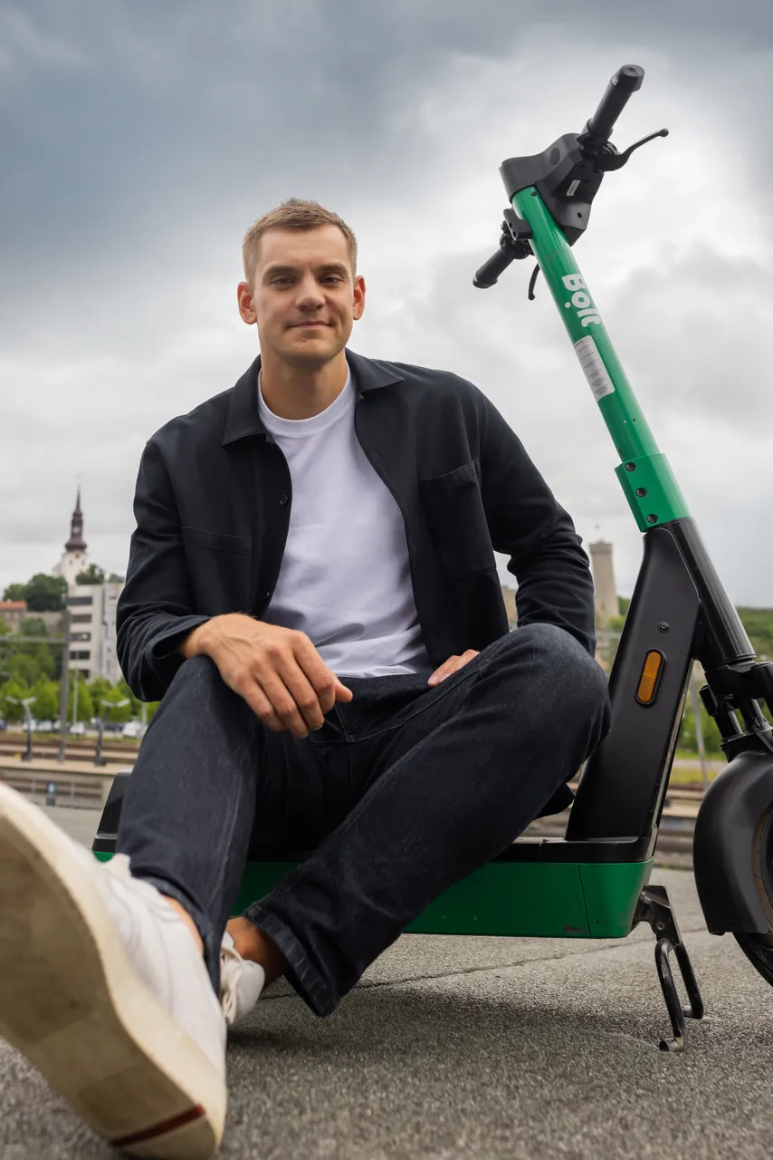 Markus Villig sitting with a Bolt e-scooter in front of Tallinn cityscape.