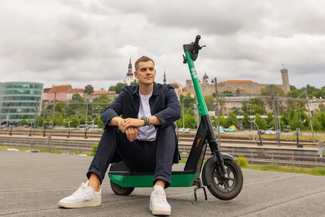 Markus Villig sitting with a Bolt e-scooter in front of Tallinn cityscape.